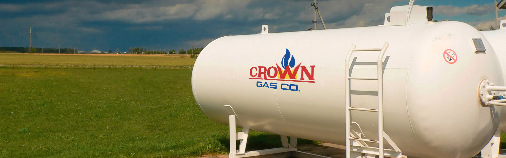 Two large, white propane tanks in the foreground with a field in the background